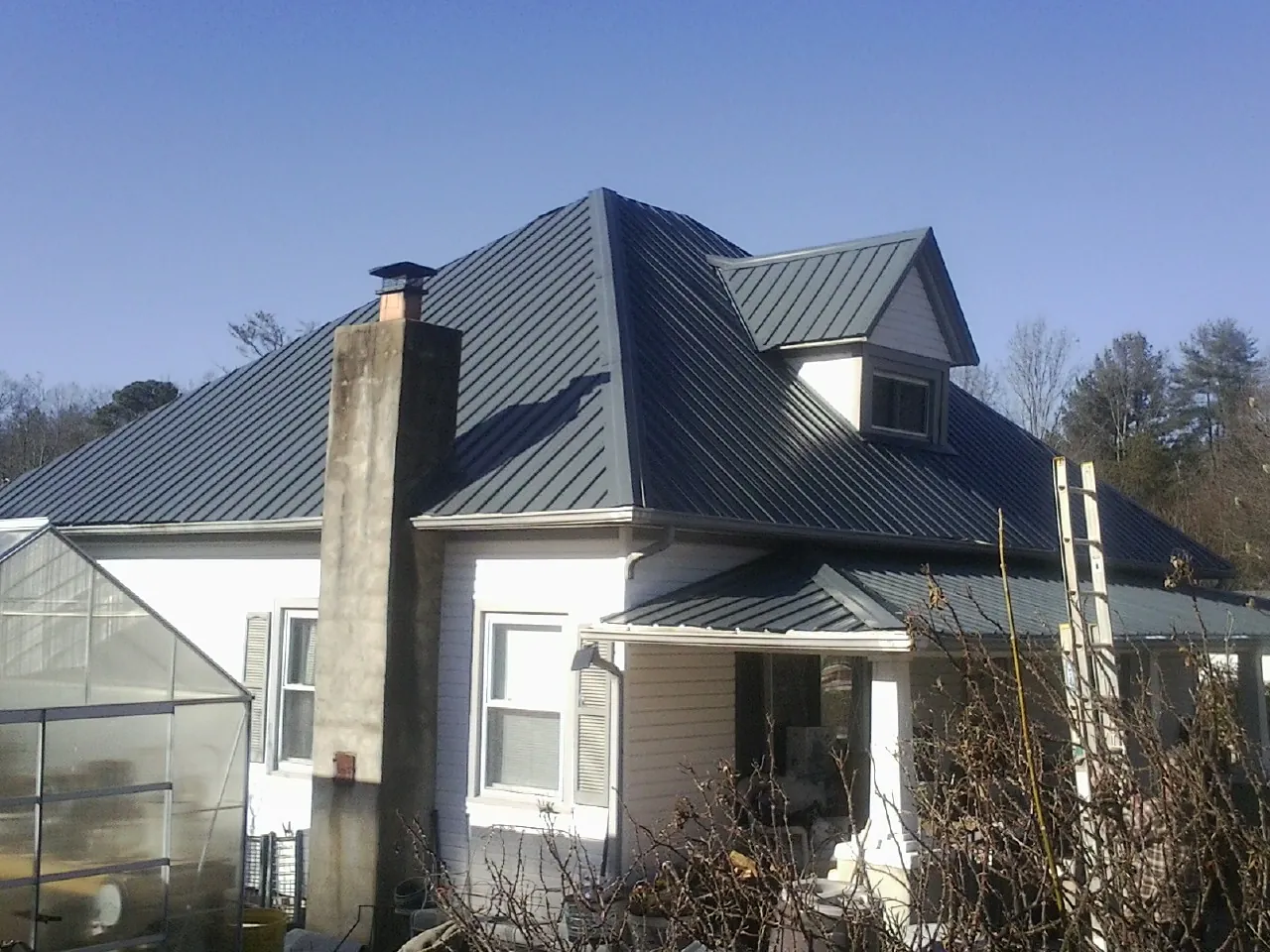 Dark blue standing seam metal roof on a white farmhouse with dormer — Slate & Tile Roof Repair by Roofing Brothers in Azalea