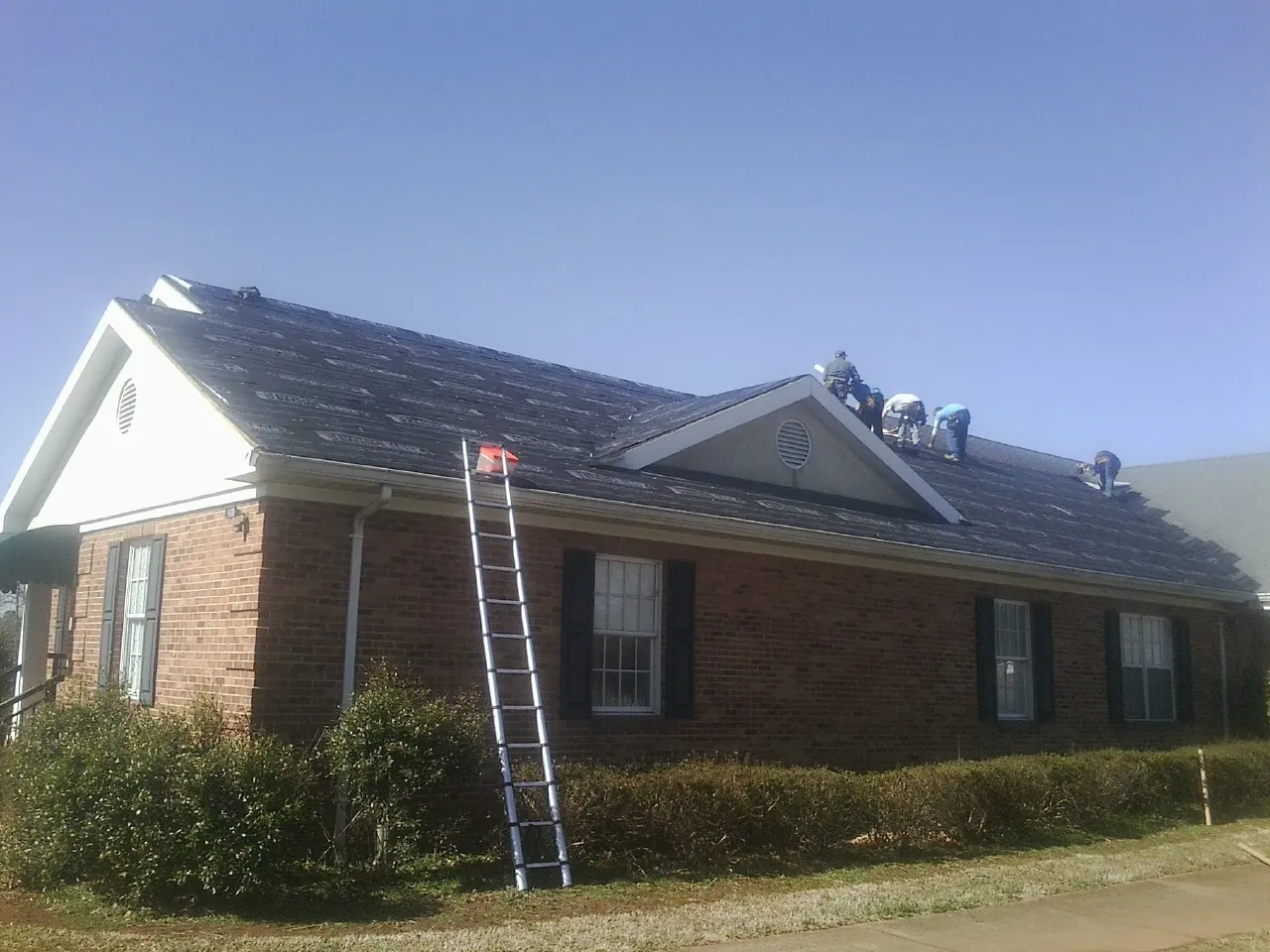 Crew tearing shingles off a brick ranch roof with a ladder set — Emergency Roof Repair work by our crew in Azalea