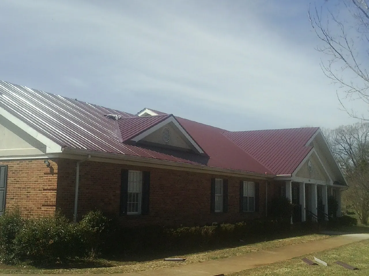 Red metal roof with gabled entries on a long brick building, from a Hail Damage Roof Repair job in Azalea