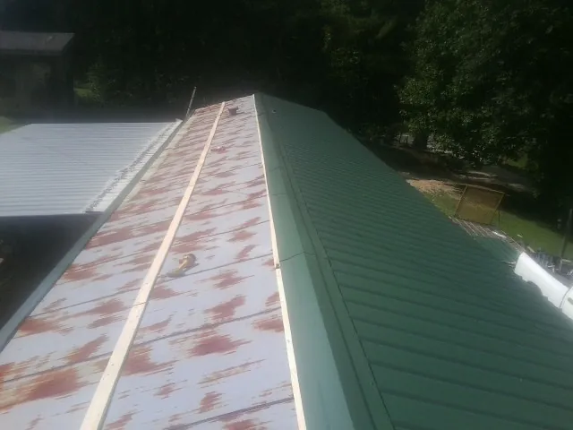 Old rusted panels beside newly installed green metal roofing — Wind Damage Roof Repair by Roofing Brothers in Azalea