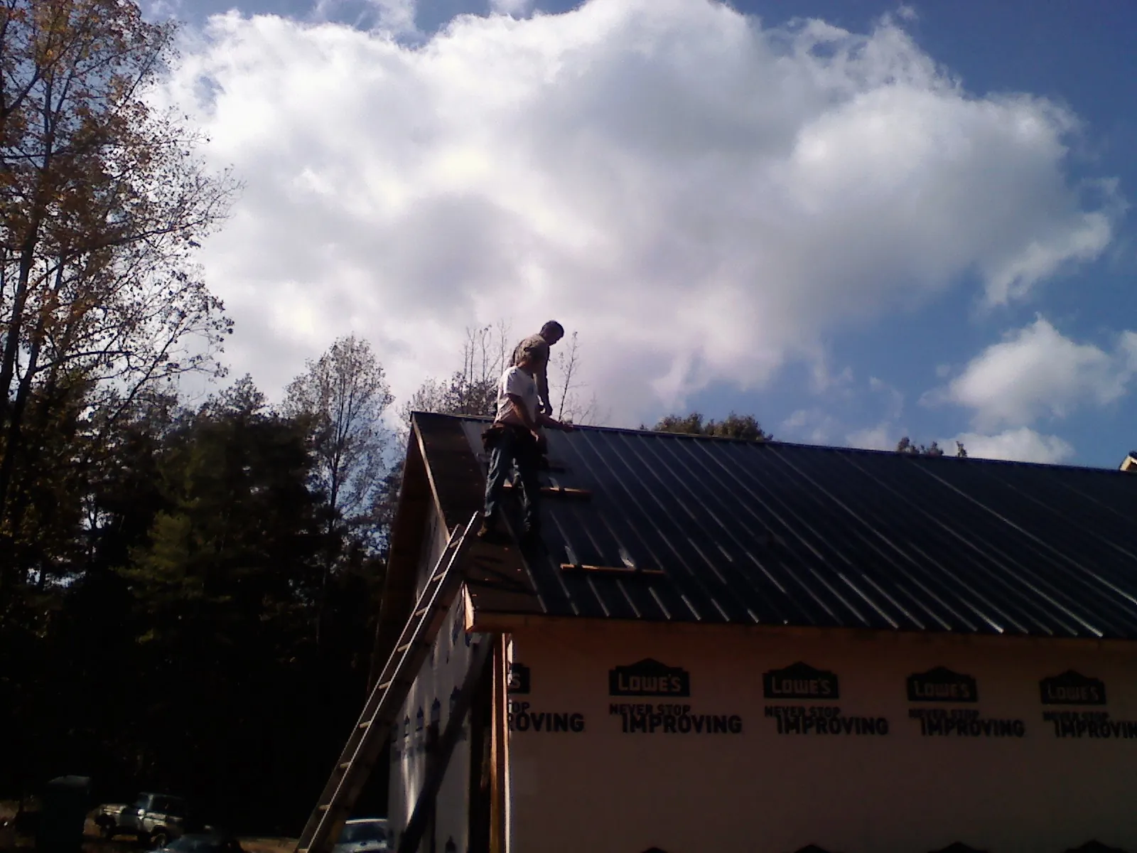 Roofer fastening dark metal panels high against a cloudy sky, from a Roof Inspection job in Azalea